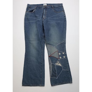 Könnte beinhalten: Blaue Jeans mit einem Patchwork-Design am unteren linken Bein. Der Patchwork-Bereich umfasst verschiedene Blautöne, weiße Sterne und ein Blumenmuster. Die Jeans haben ein klassisches Fünf-Taschen-Design.
