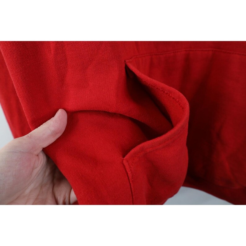 Peut inclure: Gros plan sur une poche de sweat &agrave; capuche rouge. La poche est faite d'une mati&egrave;re douce et &eacute;paisse. Le sweat &agrave; capuche est de couleur rouge uni. La poche est de style kangourou.