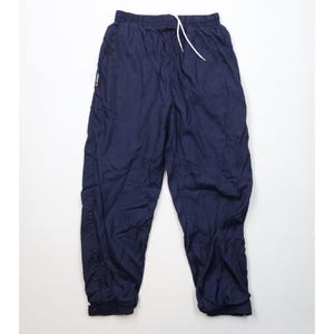 May include: Navy blue athletic pants with an elastic waistband and a white drawstring. The pants have a relaxed fit and a small logo on the left side. The cuffs are elasticated. These pants are suitable for athletic activities or casual wear.