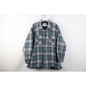 May include: A blue, black, and white plaid button-down shirt with two chest pockets. The long-sleeved shirt is hanging on a white hanger against a white background. The shirt has a collar and buttoned cuffs.