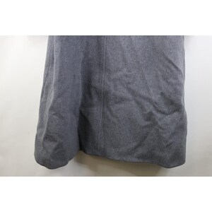 May include: A gray skirt made of a thick, textured fabric. The skirt has a slight A-line shape and a seam down the center front. The fabric appears to be a wool blend, and the skirt is unadorned.