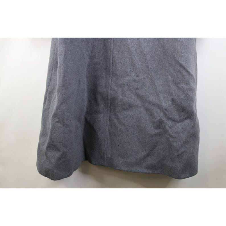 May include: A gray skirt made of a thick, textured fabric. The skirt has a slight A-line shape and a seam down the center front. The fabric appears to be a wool blend, and the skirt is unadorned.