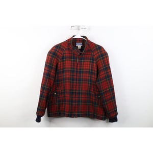 May include: A red and navy blue plaid jacket featuring a full-length front zipper, a stand-up collar, and long sleeves with dark navy blue ribbed cuffs. The jacket includes two front pockets with button closures and a Pendleton brand label inside.