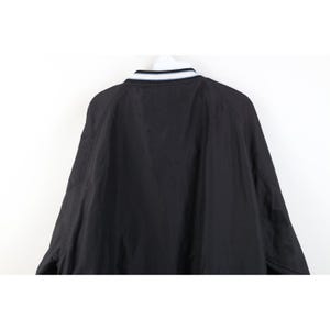 May include: Black bomber jacket with a white and navy blue striped collar. The jacket has a simple, classic design, with raglan sleeves and a smooth, matte finish. The back of the jacket is visible against a white background.
