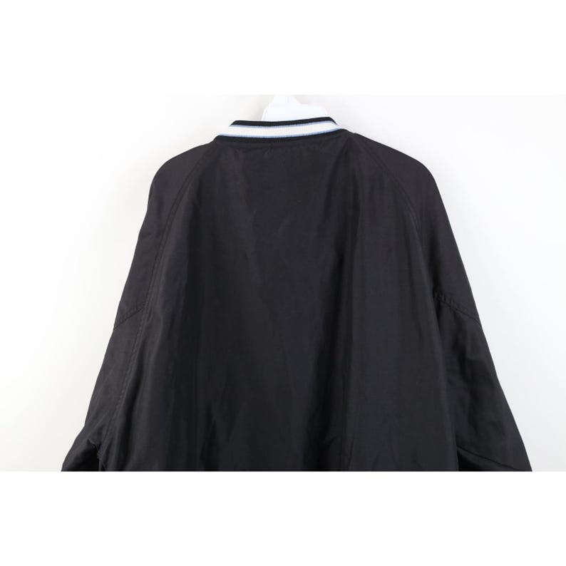 May include: Black bomber jacket with a white and navy blue striped collar. The jacket has a simple, classic design, with raglan sleeves and a smooth, matte finish. The back of the jacket is visible against a white background.