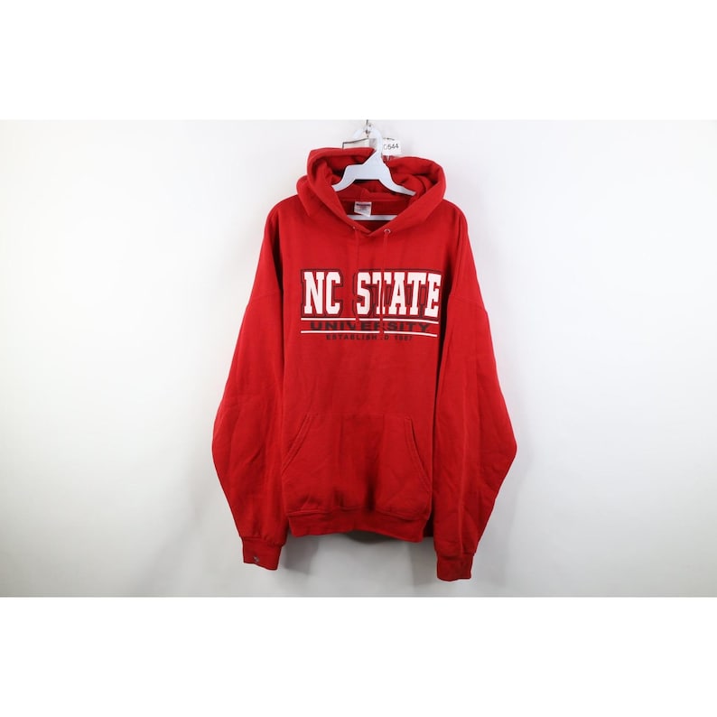 Peut inclure: Un sweat-shirt &agrave; capuche rouge avec l'inscription "NC STATE" en blanc. Le sweat-shirt a une poche avant et une capuche &agrave; cordon. Le nom de l'universit&eacute; est imprim&eacute; au-dessus de la date de cr&eacute;ation.