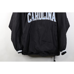 May include: Black jacket with the word "CAROLINA" in white and light blue lettering across the chest. The jacket has a drawstring at the bottom and white and blue striped cuffs.
