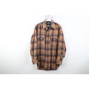 May include: A long-sleeved plaid shirt in shades of brown, orange, and navy blue. The shirt has two chest pockets and buttoned cuffs. The shirt is hanging on a white hanger.