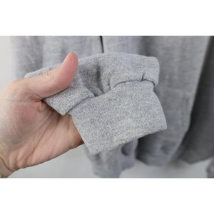 May include: A light gray long-sleeve sweatshirt featuring a ribbed knit cuff at the end of the sleeve. The fabric has a heathered texture throughout, and the garment is constructed with a soft, fleecy material consistent with casual loungewear.