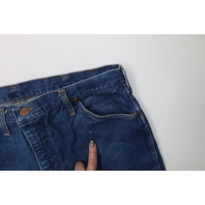Op de afbeelding: Close-up van een blauwe spijkerbroek. De jeans heeft een klassiek ontwerp met vijf zakken, met een knoop- en ritssluiting. De denim is een medium wassing en de jeans lijken vintage te zijn.