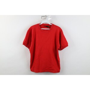 May include: A solid red short-sleeve t-shirt with a crew neckline. The shirt is displayed on a white plastic hanger against a plain white background. The fabric appears to be a standard cotton knit with ribbed detailing at the collar and sleeve cuffs.