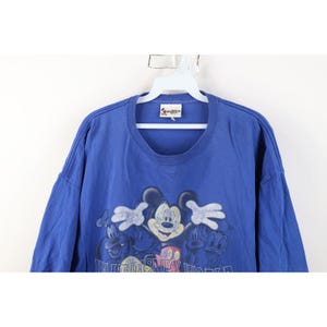 May include: Blue t-shirt featuring Mickey Mouse, Donald Duck, and Goofy. The graphic includes the text "Walt Disney World". The shirt is hanging on a white hanger.