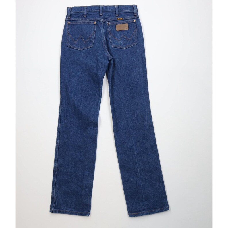 K&ouml;nnte beinhalten: Dunkelblaue Jeans aus Denim mit klassischem F&uuml;nf-Taschen-Design. Merkmale sind ein brauner Lederaufn&auml;her und das Wrangler-Logo. Die Jeans haben einen geraden Beinverlauf.