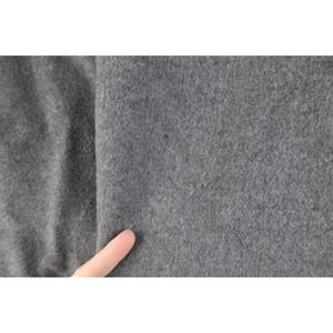May include: Close-up of a gray fabric with a soft, textured surface. The fabric appears to be a solid color, with a slight variation in tone. A finger is touching the fabric.