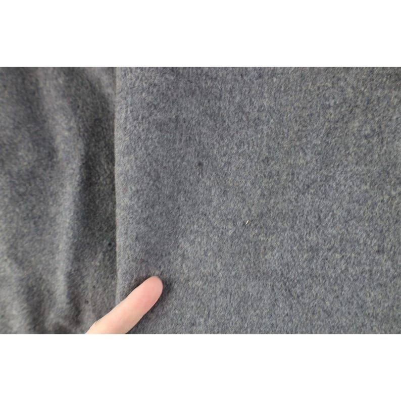 May include: Close-up of a gray fabric with a soft, textured surface. The fabric appears to be a solid color, with a slight variation in tone. A finger is touching the fabric.