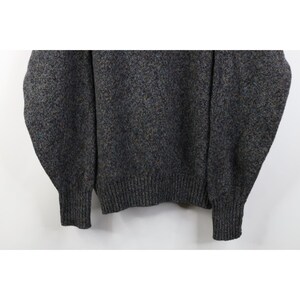 May include: A gray sweater with a speckled pattern. The sweater has a ribbed hem and cuffs. The fabric appears to be a blend of gray, brown, and blue yarns, creating a textured look. The sleeves are long and the overall style is casual.