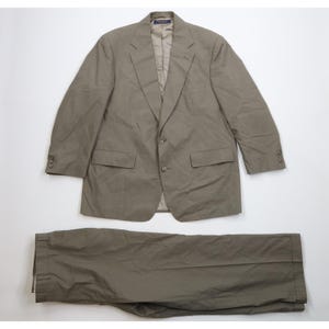May include: A two-piece suit in a muted olive green color. The jacket has a two-button closure, notched lapels, and two front pockets. The matching trousers are neatly folded below the jacket. The suit is made of a lightweight fabric.