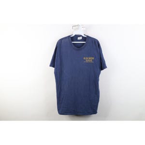 Könnte beinhalten: Ein marineblaues Kurzarm-T-Shirt mit Rundhalsausschnitt. Auf der Vorderseite des Shirts befindet sich der Text RUSH WEEK 2002, der in goldener Schrift im oberen linken Brustbereich aufgedruckt ist. Das Kleidungsstück hängt an einem weißen Kunststoffbügel.