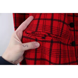 Peut inclure: Gros plan sur une veste &agrave; carreaux rouge et noir. La veste pr&eacute;sente un motif &agrave; carreaux classique avec des boutons noirs et une poche. Le tissu semble &ecirc;tre de la laine &eacute;paisse ou un m&eacute;lange de laine, adapt&eacute; au temps froid.