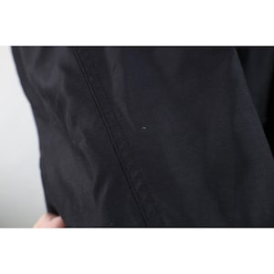 May include: Close-up of black fabric with a visible seam running vertically. The fabric appears to be a solid color, possibly a garment or textile. The image is well-lit, highlighting the texture and details of the material.