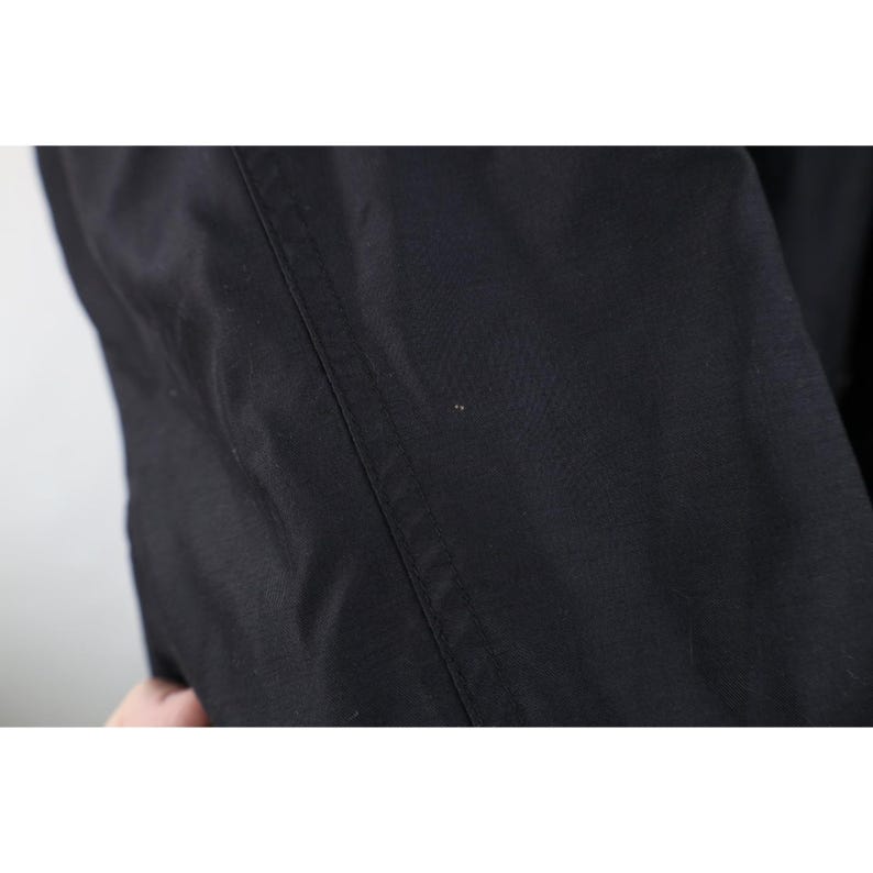 May include: Close-up of black fabric with a visible seam running vertically. The fabric appears to be a solid color, possibly a garment or textile. The image is well-lit, highlighting the texture and details of the material.