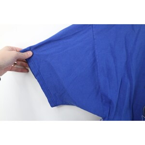 May include: A close-up of a royal blue t-shirt sleeve. The sleeve is made of a soft, lightweight fabric. The sleeve is being held by a hand.