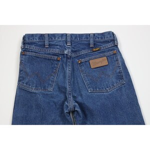 Puede incluir: Vaqueros azules de mezclilla con el logo de Wrangler en el bolsillo trasero. Los vaqueros tienen un estilo cl&aacute;sico de cinco bolsillos, cierre de bot&oacute;n y cremallera, y trabillas para el cintur&oacute;n. Los bolsillos traseros presentan las costuras Wrangler.