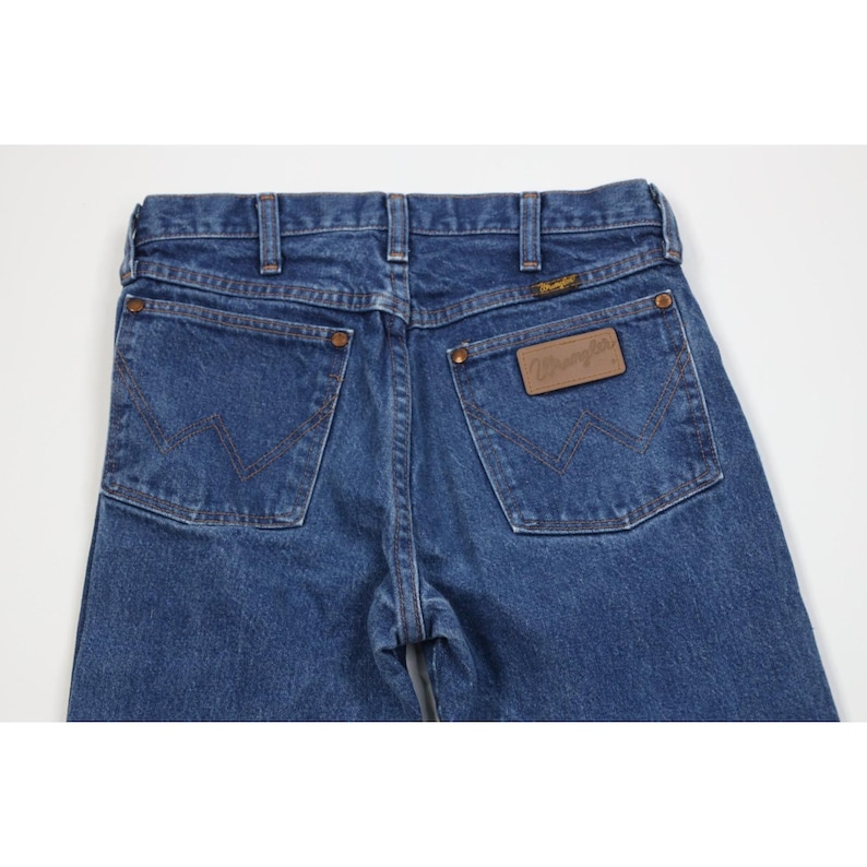 Puede incluir: Vaqueros azules de mezclilla con el logo de Wrangler en el bolsillo trasero. Los vaqueros tienen un estilo cl&aacute;sico de cinco bolsillos, cierre de bot&oacute;n y cremallera, y trabillas para el cintur&oacute;n. Los bolsillos traseros presentan las costuras Wrangler.