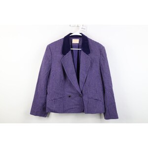 May include: A purple and white houndstooth blazer with a navy blue velvet collar. The blazer has a single-button closure and two front pockets. The jacket is hanging on a white hanger.