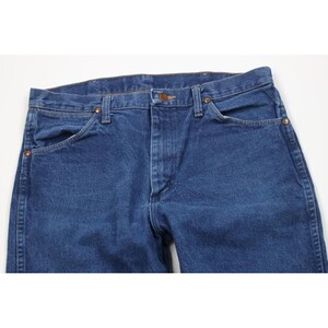 May include: Close-up of blue denim jeans. The jeans have a classic five-pocket design with a button and zipper closure. The denim is a medium wash, and the jeans appear to be new or in excellent condition.