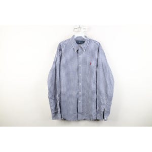 May include: A long-sleeve button-down shirt featuring a blue and white gingham check pattern. The shirt includes a button-down collar, a front button placket, and a small red embroidered logo on the left chest area. It is displayed on a white hanger.