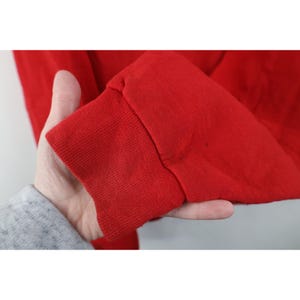 Peut inclure: Gros plan sur une manche de sweat-shirt rouge. Le poignet est c&ocirc;tel&eacute; et le tissu semble &ecirc;tre un tricot &eacute;pais. La manche est tenue par une personne.