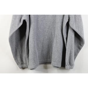 May include: A heather gray fleece pullover sweatshirt. The long sleeves have elastic cuffs, and the bottom hem is also elastic. The fabric has a soft, textured appearance. The sweatshirt is a casual style.