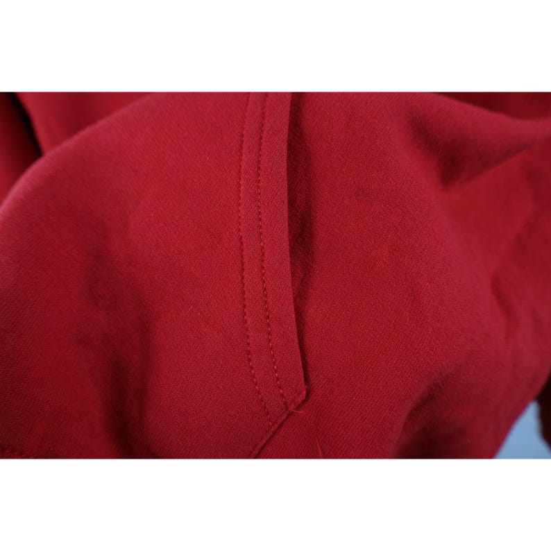 Peut inclure: Gros plan sur une poche de sweat &agrave; capuche rouge avec des coutures visibles. Le tissu est d'un rouge uni et profond, et la poche est cousue avec un fil contrastant. La texture du tissu est douce et l&eacute;g&egrave;rement textur&eacute;e.