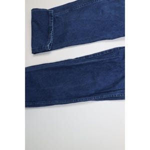 May include: Close-up of a pair of dark blue denim jeans. The jeans are folded at the cuff, showing the detailed stitching. The fabric has a classic, slightly faded appearance.