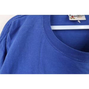May include: Close-up of a blue t-shirt with a crew neck. The shirt has a tag that reads "Walt Disney World". The shirt is hanging on a white hanger.