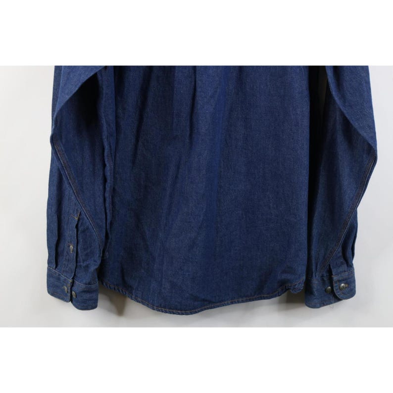 May include: A dark blue denim shirt with long sleeves. The shirt has buttoned cuffs and a button-down front. The fabric appears to be a medium weight denim, suitable for casual wear. The shirt is hanging against a white background.