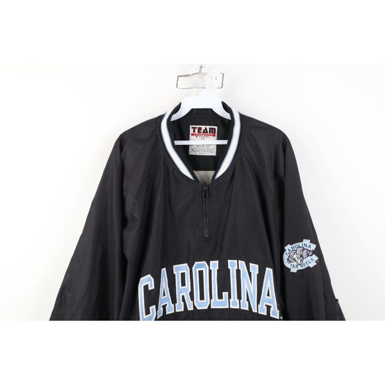 May include: Black pullover jacket with a white and light blue collar and the word "CAROLINA" across the chest in light blue lettering. The jacket has a small logo on the right sleeve.