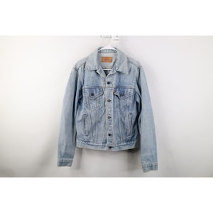 May include: Light blue denim jacket with a classic design. Features a button-up front, two chest pockets, and two side pockets. The jacket has a faded look and a small red tag on the chest pocket. A timeless piece of outerwear.