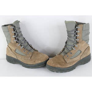 Puede incluir: Un par de botas tácticas de ante color canela y lona verde oliva con caña alta, cordones grises, ojales metálicos y suelas gruesas de goma negra. Las botas tienen una puntera reforzada y un diseño estructurado con cuello acolchado.