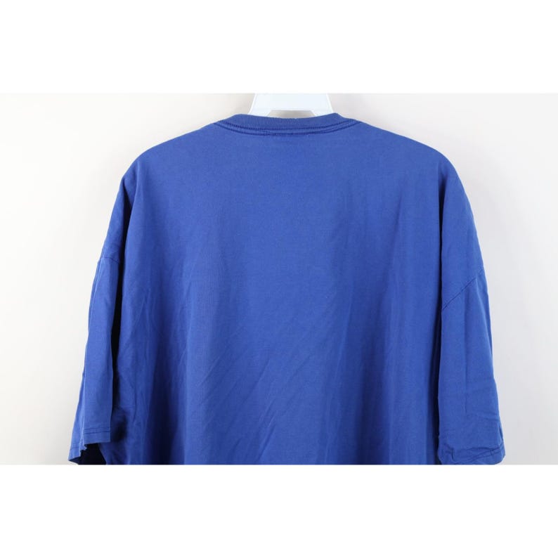 May include: A solid blue t-shirt, hanging on a white hanger. The shirt is made of a soft material and has a crew neck. The sleeves are short and wide. The shirt is a vibrant shade of blue.
