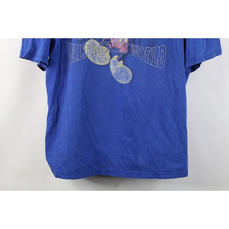 May include: A blue t-shirt featuring the text "WALT DISNEY WORLD" in a stylized font, with Mickey Mouse ears. The shirt is a solid blue color and appears to be made of cotton.