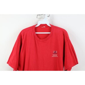 May include: A red t-shirt with a crew neck and short sleeves. The shirt features a small logo on the upper left chest that reads "US Soccer Coaches Organization". The shirt is made of a soft, likely cotton material.
