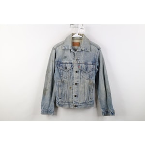 May include: Light blue denim jacket with button closures, two chest pockets, and two side pockets. The jacket has a classic collar and a distressed appearance. The jacket is hanging on a white hanger.