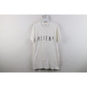 May include: A white short-sleeve t-shirt featuring the black text ALIEN 3 printed across the chest. The shirt has a crew neckline and a standard fit, with the graphic positioned centrally on the front of the garment. The fabric appears smooth.
