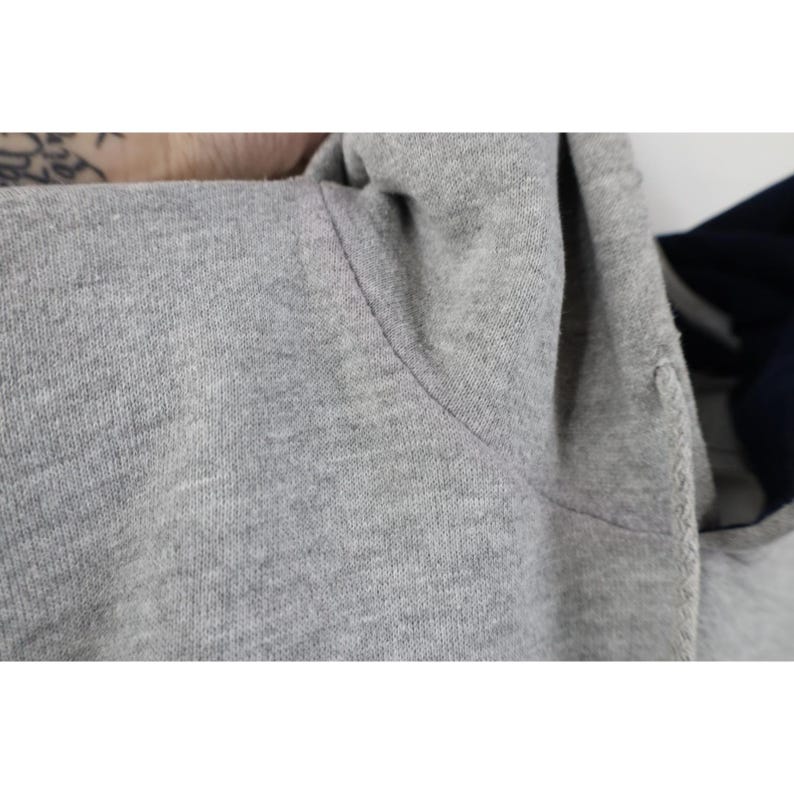 May include: A heather gray hooded sweatshirt featuring a dark navy blue interior lining within the hood. The garment is constructed from a soft, textured knit fabric with visible stitching along the shoulder seam and a matching gray drawstring.