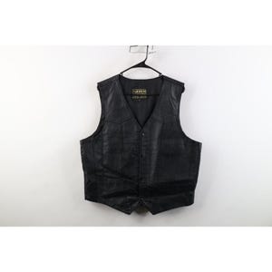 Può includere: Un gilet in pelle nera con scollo a V, chiusura frontale con bottoni e due tasche anteriori. L'etichetta interna riporta la scritta Hudson Leather. Il capo è appeso a una gruccia di plastica nera su uno sfondo bianco uniforme.