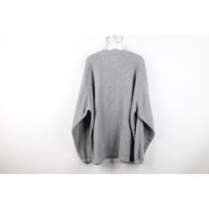 May include: A heather gray sweatshirt hangs on a white hanger against a white background. The long-sleeved sweatshirt has a crew neck and ribbed cuffs and hem. The fabric appears to be a soft, fleece-like material.