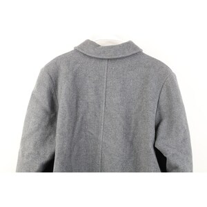 May include: A gray wool coat, viewed from the back, with a classic collar and a center seam. The coat is hanging on a white hanger. The fabric has a subtle texture.