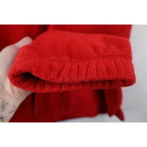 May include: Close-up of a bright red fleece jacket sleeve. The cuff is ribbed and the fabric has a soft, textured appearance. The sleeve is slightly bunched at the cuff.